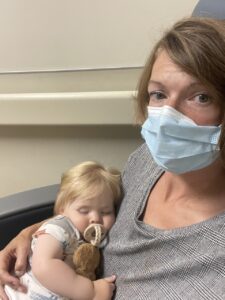 Mom and baby sitting in a hospital, mom is wearing a mask, baby is sucking on a soother sleeping